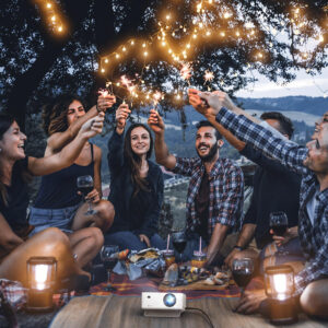 Seven young friends sitting outdoors lighting firecrackers with a projector next to them