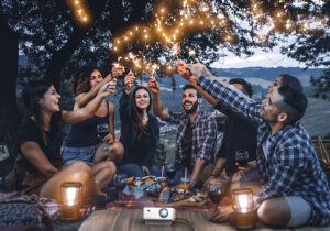 Seven young friends sitting outdoors lighting firecrackers with a projector next to them.