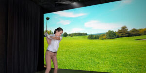 Woman taking a golf swing against a screen displaying a virtual golf course.