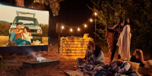 6 friends watching a movie on a projector outdoors while camping.